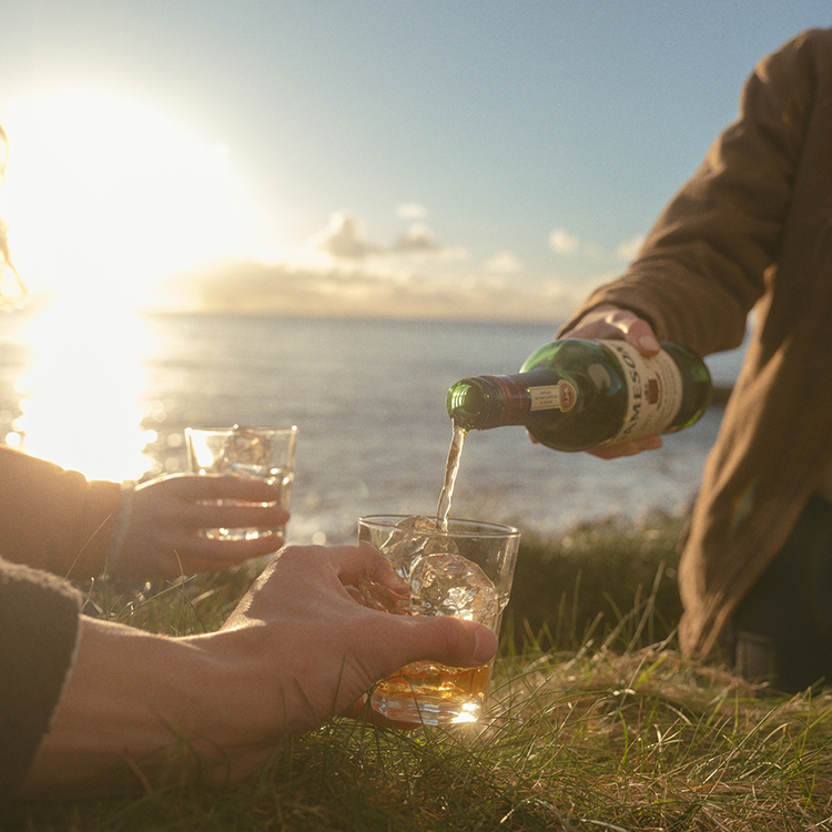 Friends enjoying a Jameson Irish Whiskey on the rocks overlooking the sea and sunset