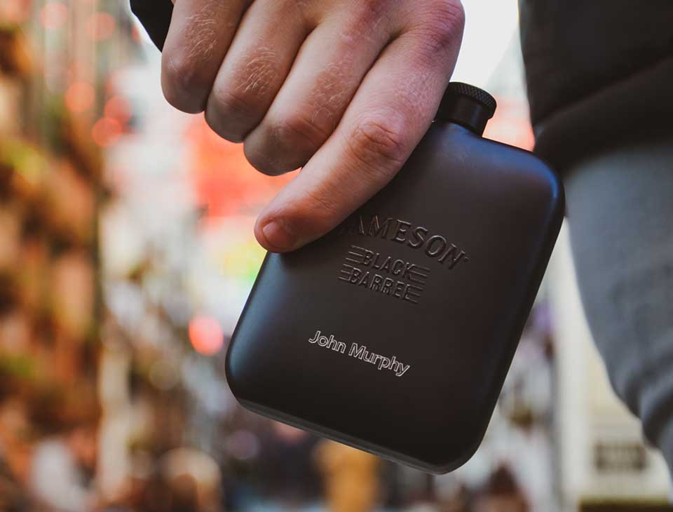 A man holding a personalised Jameson Black Barrel hip flask with John Murphy engraved onto it