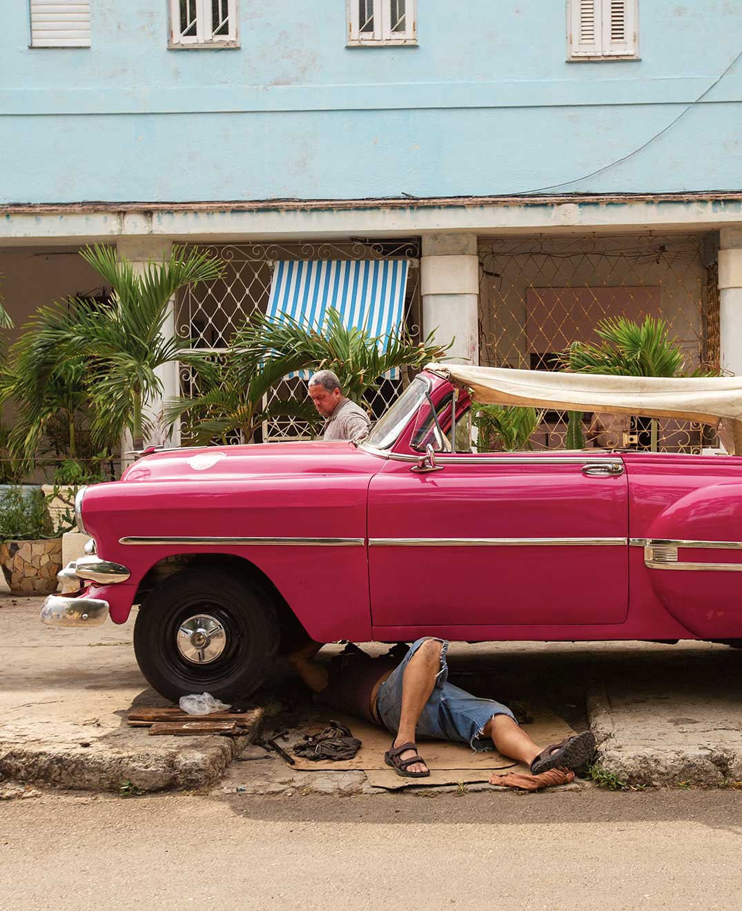 two men fixing a pink vintage car on the streets of cuba