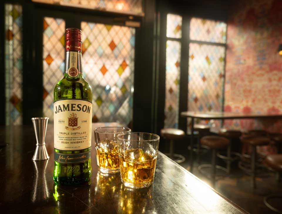 jameson irish whiskey bottle alongside two whiskey on the rocks servings