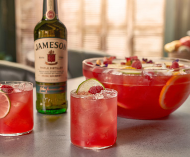 A picture of a bowl of fruity pink punch with two tumbler glasses and a bottle of Jameson Original