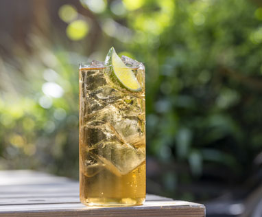 A tall glass of Jameson, Ginger and Lime cocktail in outdoor setting in summer time